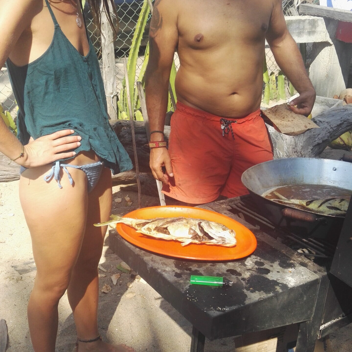 two people in swim ware grilling fish on the beach