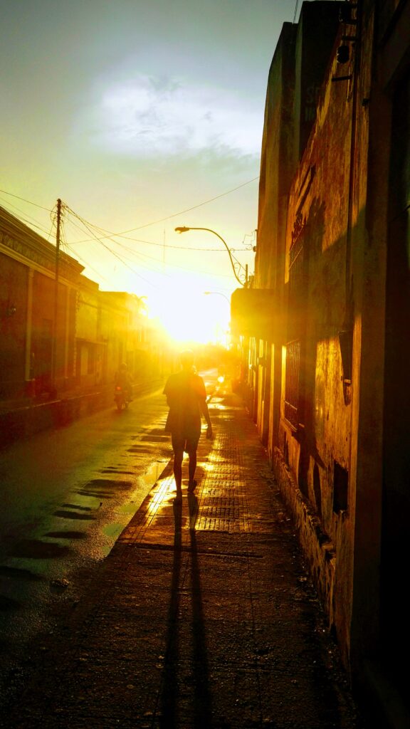 sunset shining through the empty streets of, person walking towards it