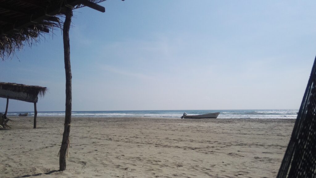 lonely beach palapa constructs reaching in a single boat on the sand calm ocean under blue sky