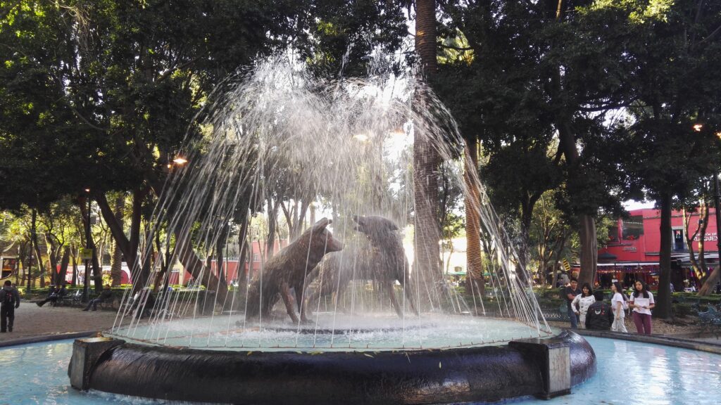fountain with two coyotes playing in a cage of water