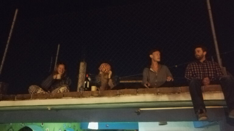 four people sitting at the edge of the roof chilling, looking around, drinking from cups